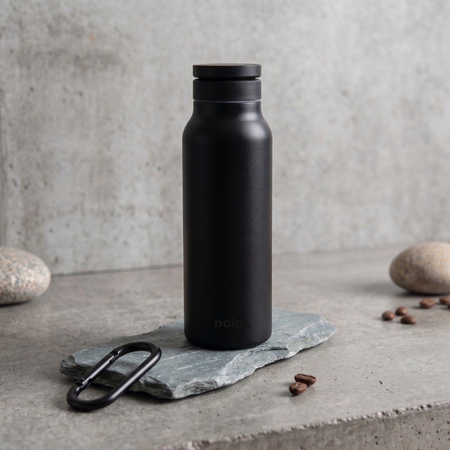 Carbon magnetic water bottle with phone holder styled on stone surface in a modern, minimal setting